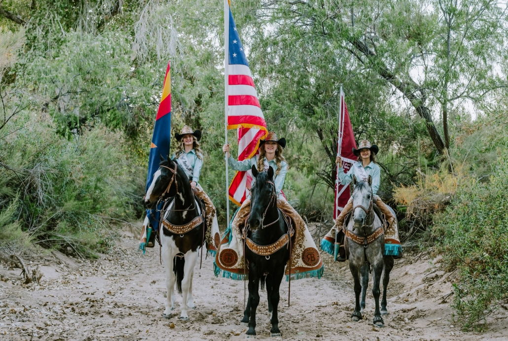 The 2026 Roots N Boots Pro Rodeo Royalty Court stands on horseback, facing the camera holding the American flag, Arizona flag.