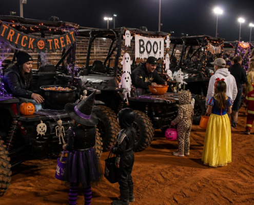 Children in Halloween costumes trick or treating at the Horseshoe Harvest Hangout Trunk or Treat Side-by-Side Candy Loop inside the arena at Horseshoe Park & Equestrian Centre in Queen Creek, AZ — decorated side by sides with candy, Halloween decorations, and festive lighting. October 31, 2026.